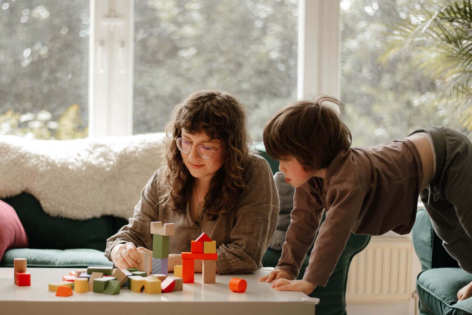 Mama spielt im Wohnzimmer mit ihrem Sohn. Es sind viele bunte Bausteine auf dem Sofatisch.