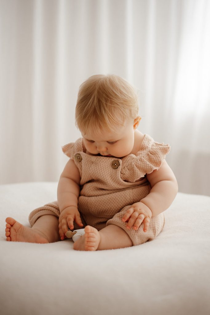 Baby sitzt auf Sitzkissen und spielt mit einer Maus aus Holz.