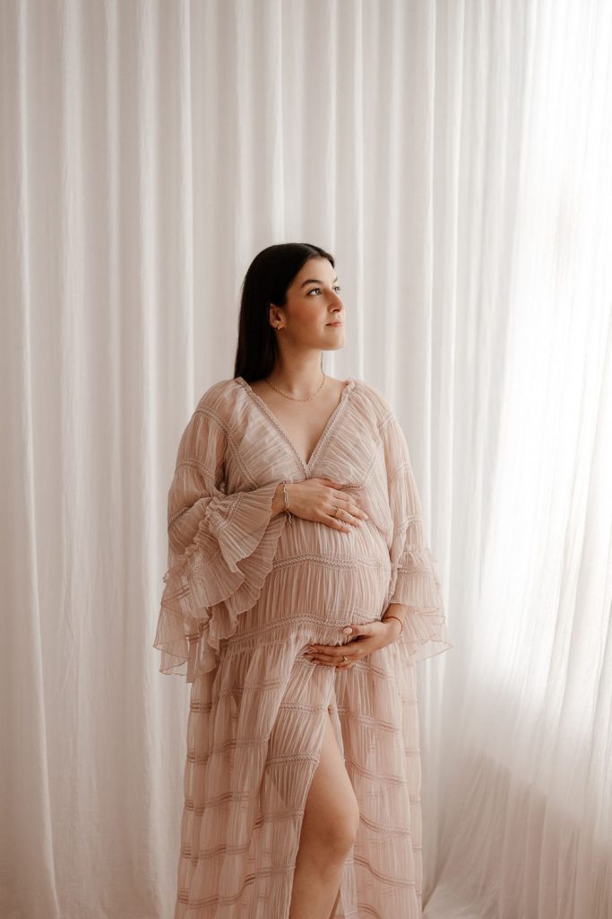 Schwangere mit Maxikleid. Hände auf dem Babybauch während eines Babybauchshootings in der Nähe von Neumünster.