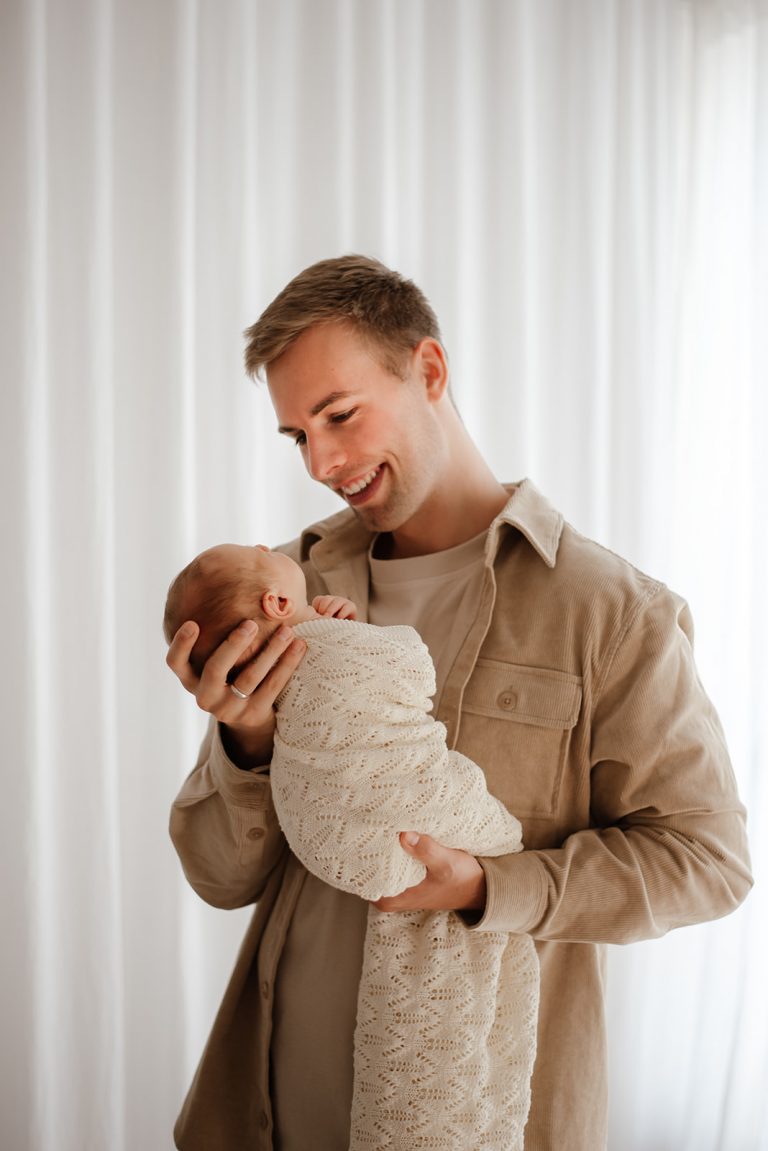 Papa hält sein Neugeborenes liebevoll im Arm und schenkt ihm Geborgenheit bei einem natürlichen Babyshooting nahe Neumünster.