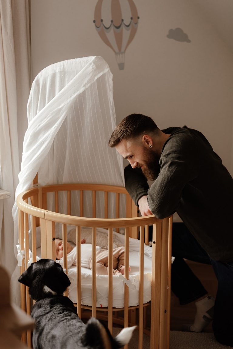 Papa betrachtet sein schlafendes Baby voller Liebe und Verbundenheit im Familienalltag bei einer authentischen Homestory in Kiel.